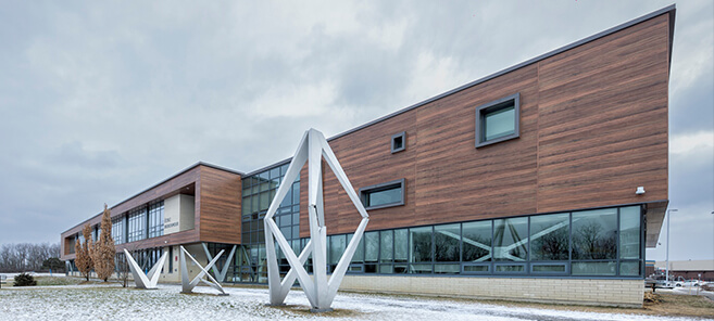 Intérieur d'une école secondaire avec gradins en bois, grande fenestration et aire de rassemblement lumineuse.